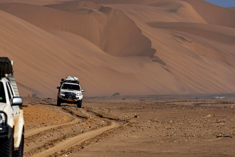 Two overland 4x4s on a sandy track, Namib dunes behind