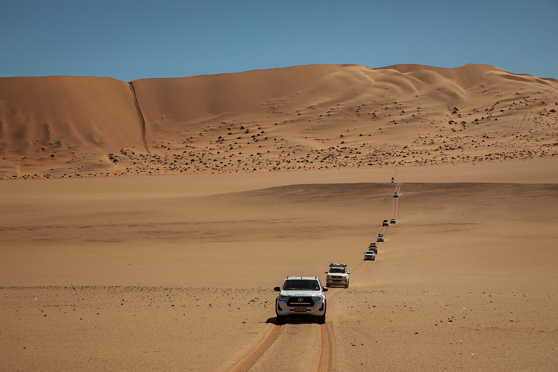Convoy approaching red dunes, ant-scale