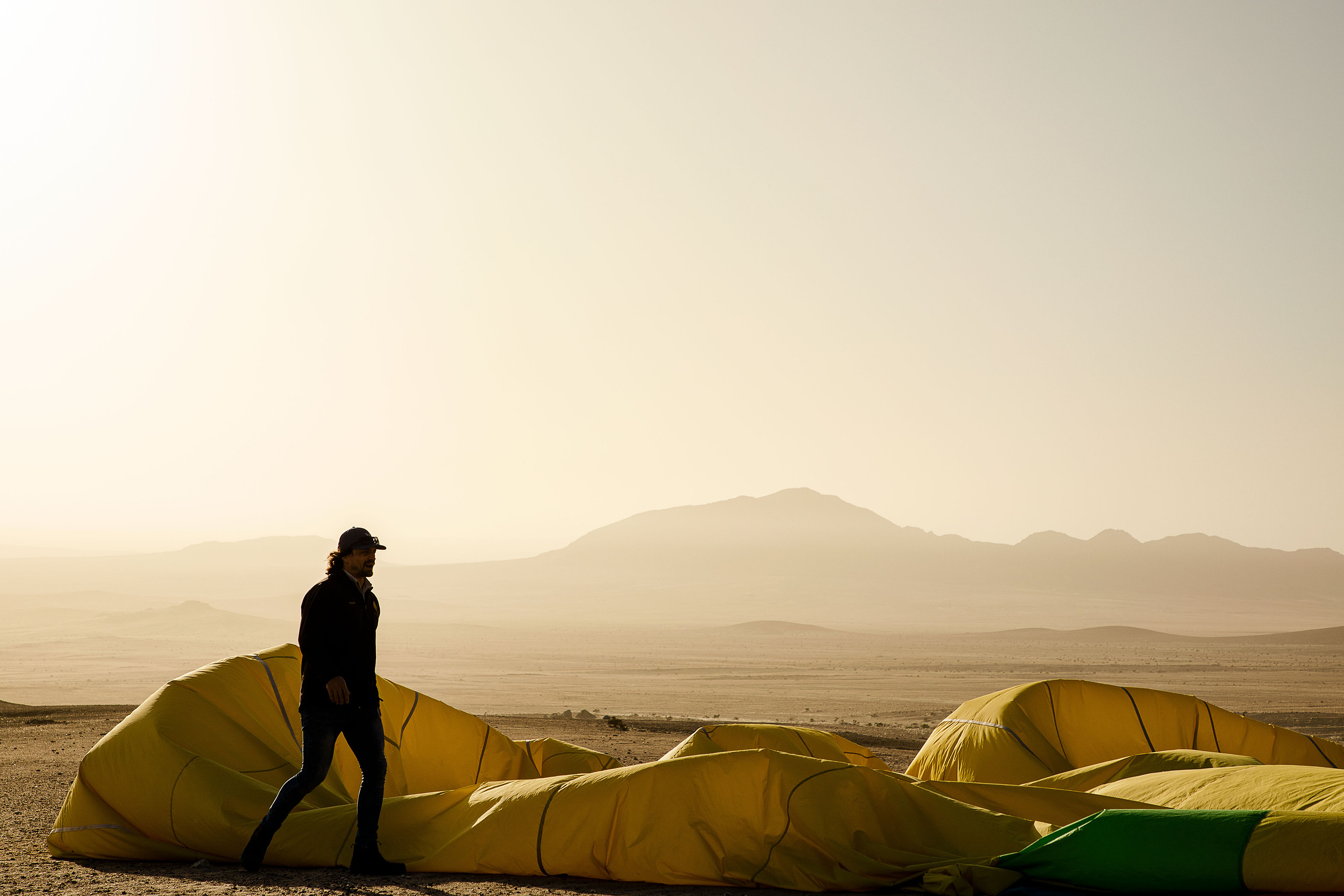 Production action — figure walking past hot-air balloon at sunrise, Namib